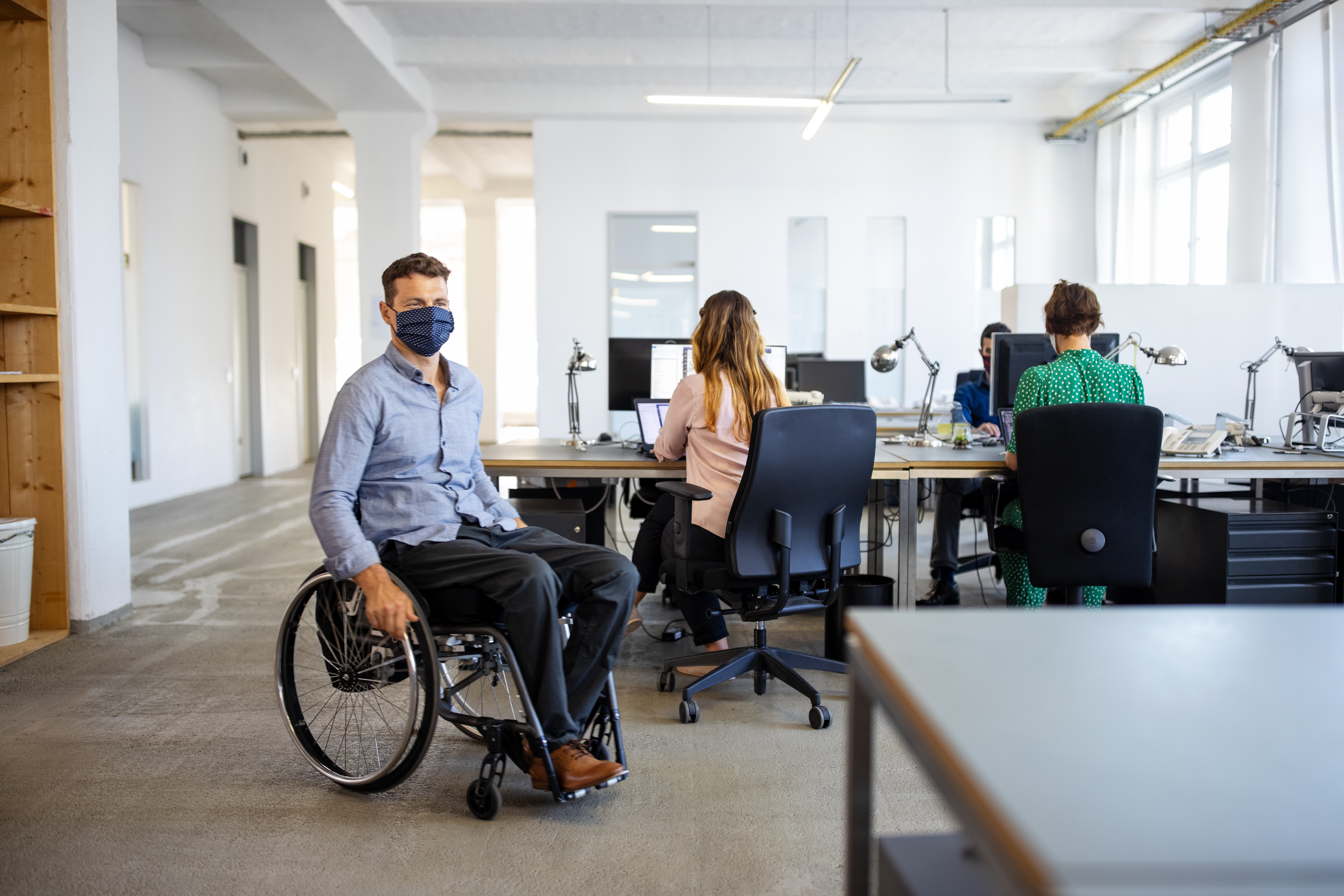 Businessman in wheelchair arriving at work. Man with disability wearing face mask in office.