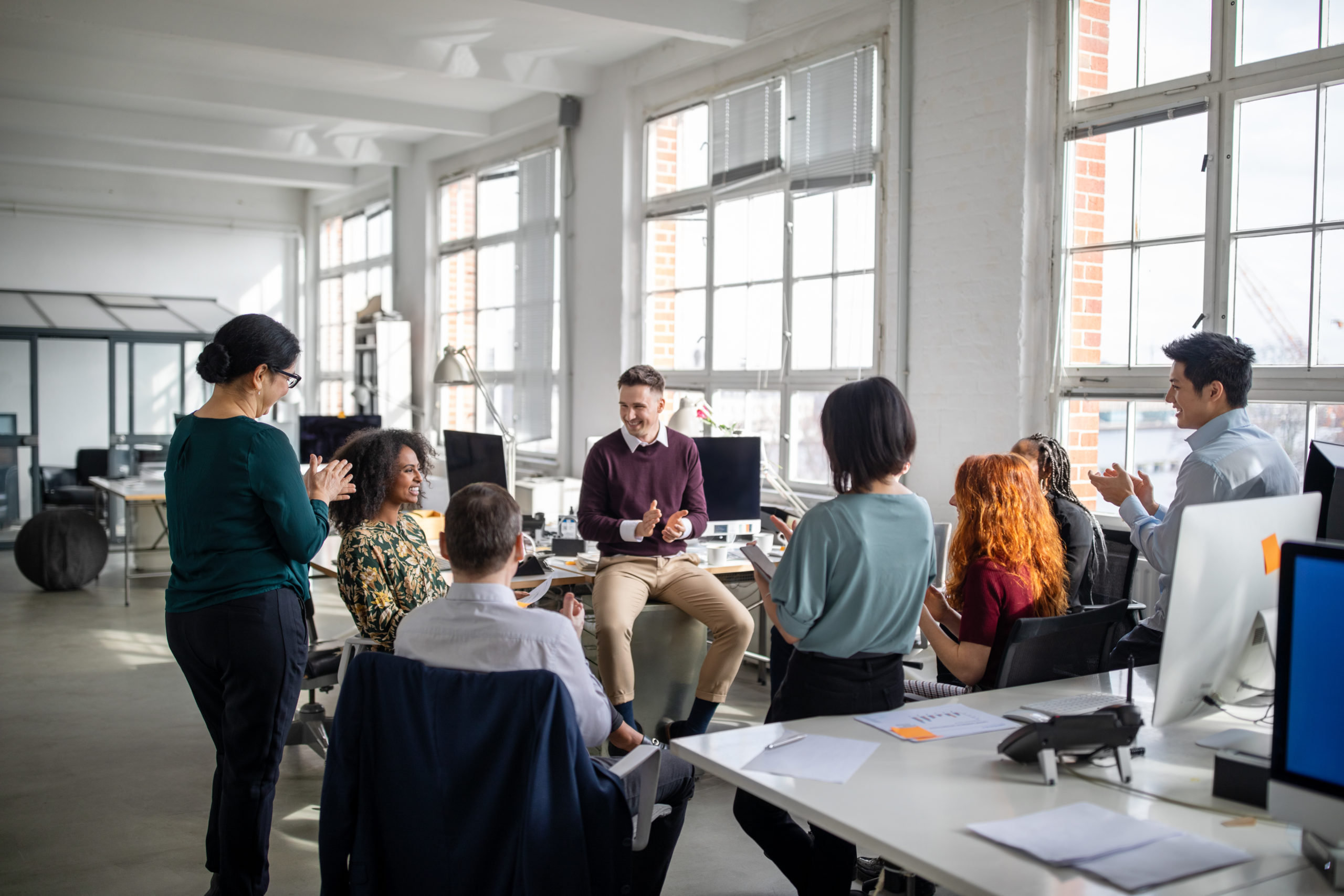 Group of business people clapping hands for a coworker in staff meeting. Multi-ethnic business team applauding for a female colleague in a meeting.