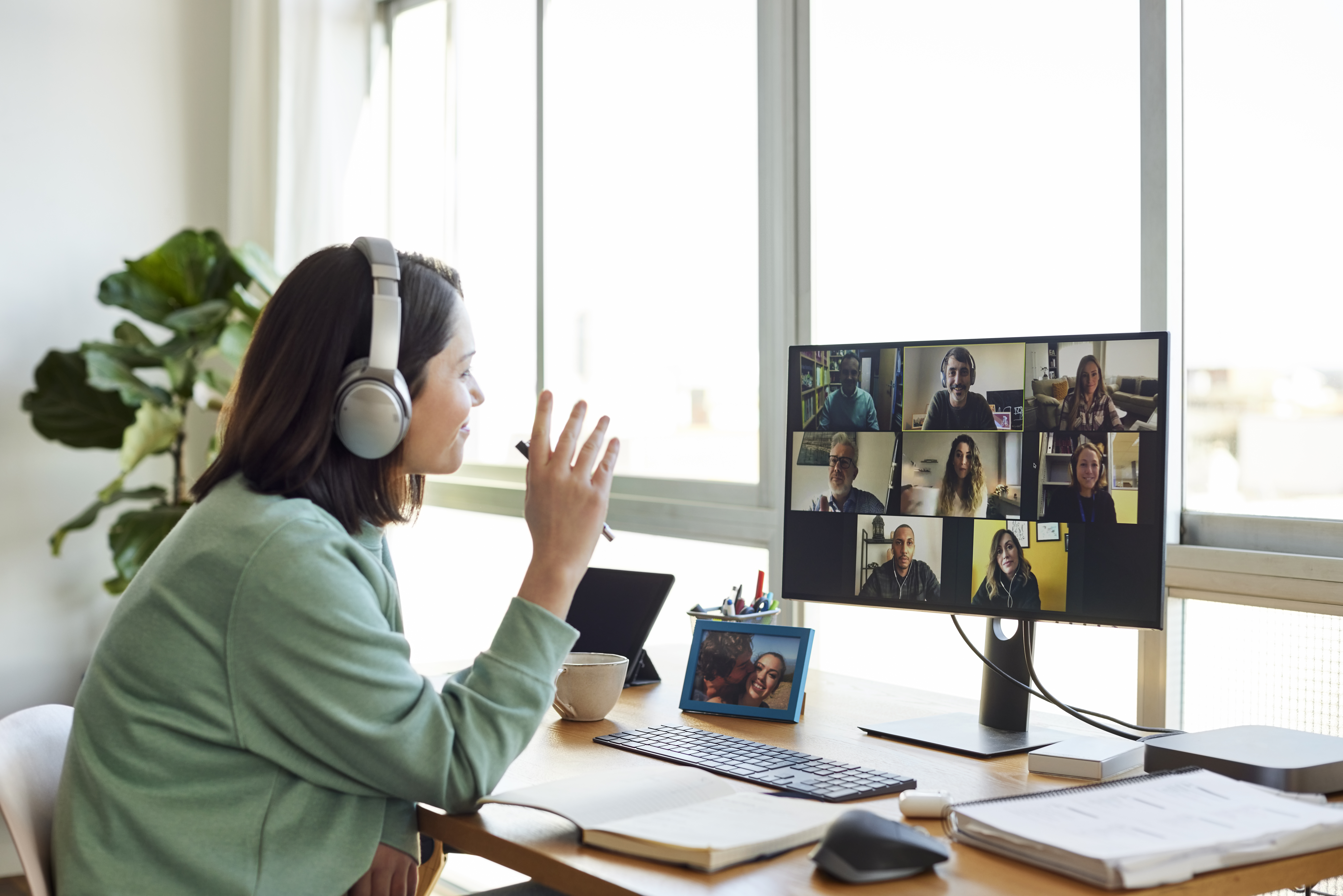 Female entrepreneur discussing with colleagues on video call. Businesswoman is sitting at table in home office. She is wearing headphones.