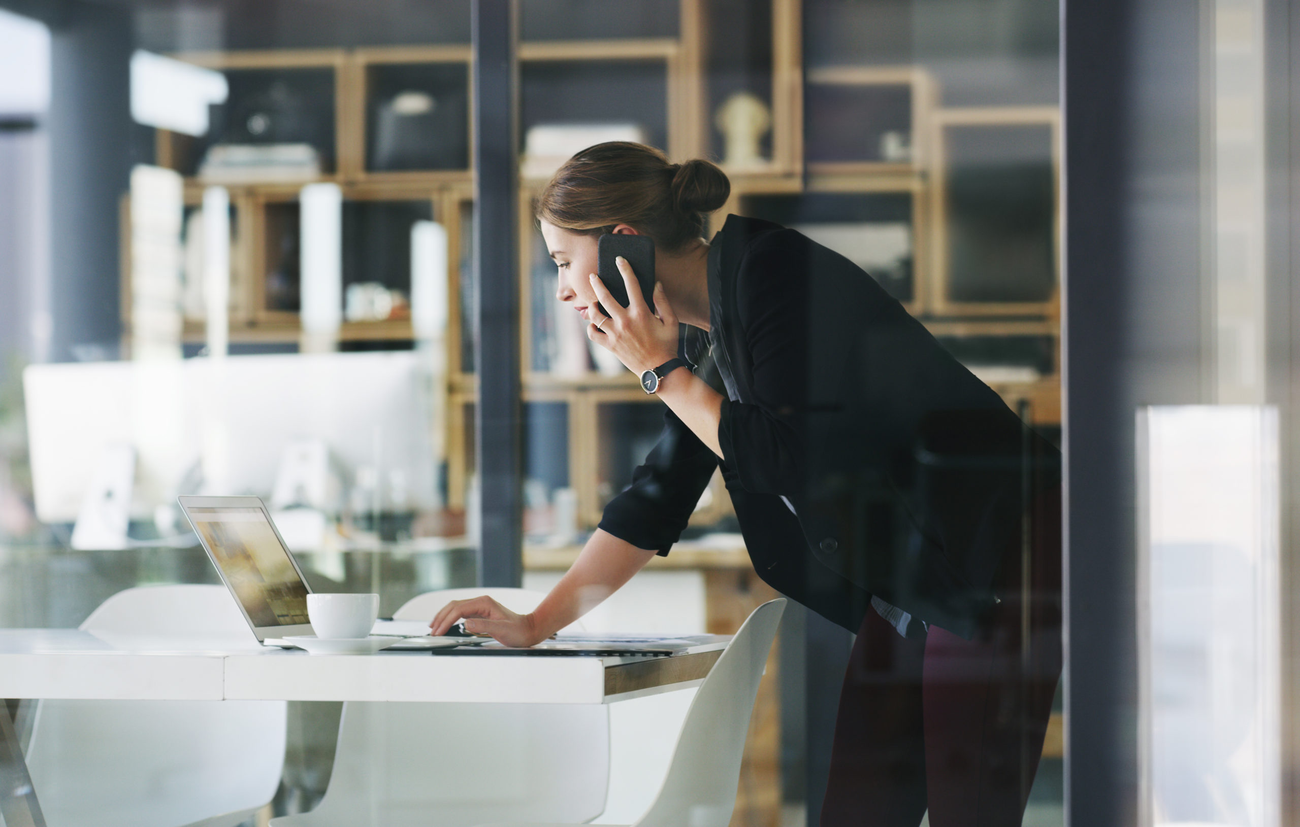 Cropped shot of an attractive young businesswoman talking on her cellphone and typing on her laptop in the office