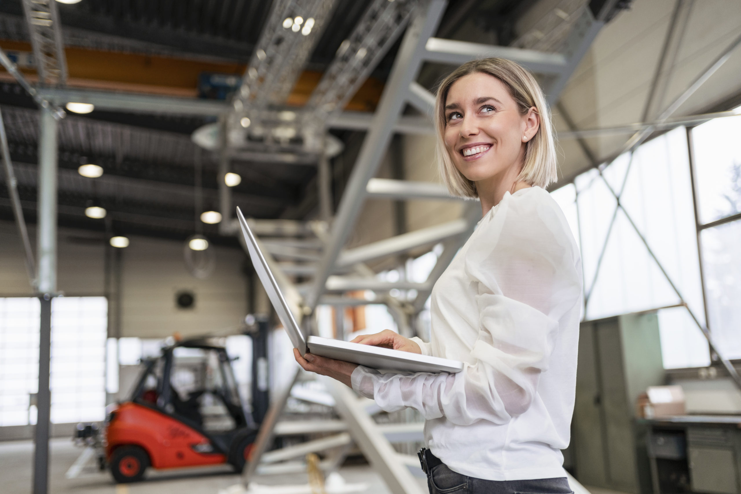 Smiling young woman using laptop in a factory