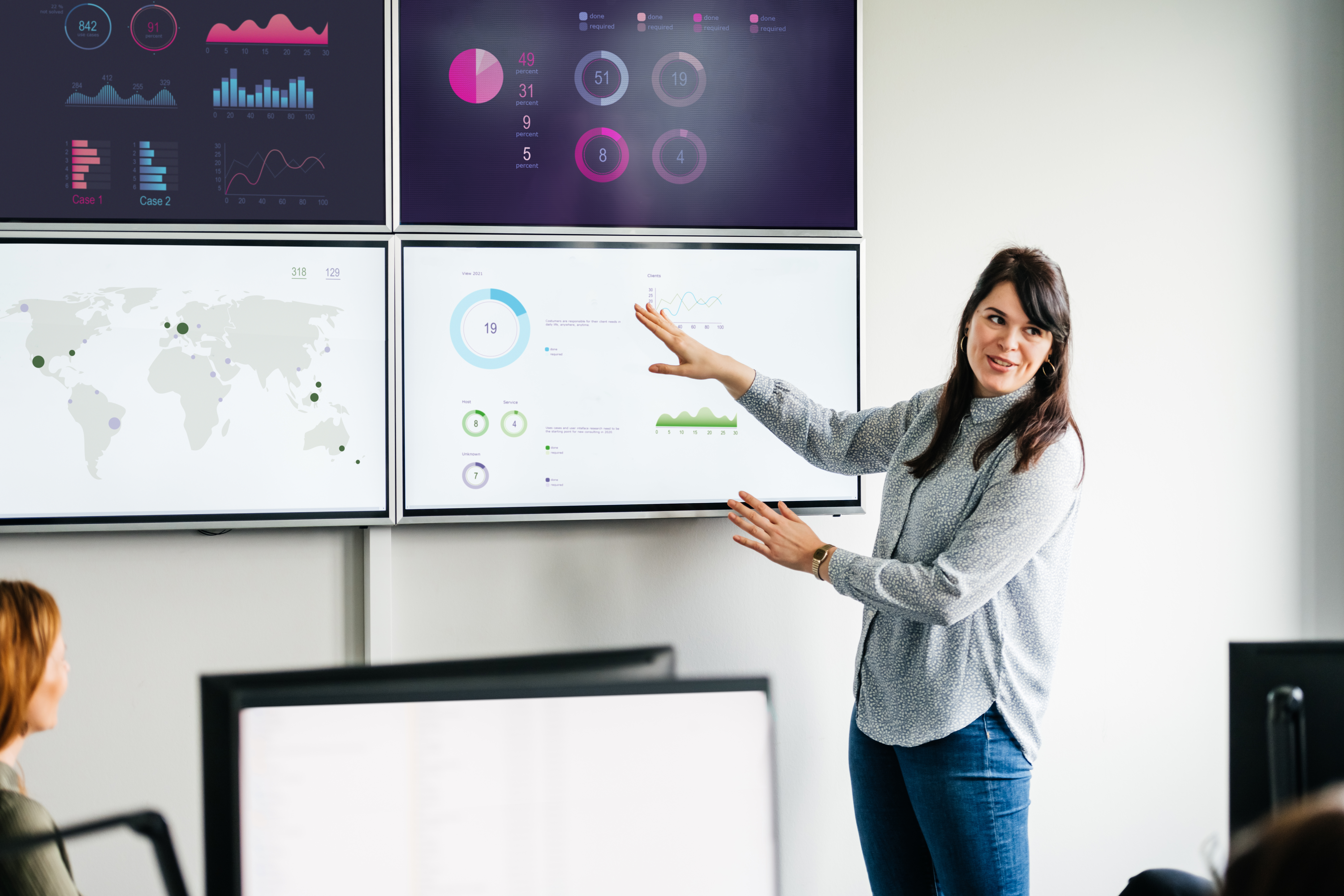 A businesswoman explaining series of graphs and data sets displayed on some large, wall mounted monitors in the office to get executive buy-in for HR.