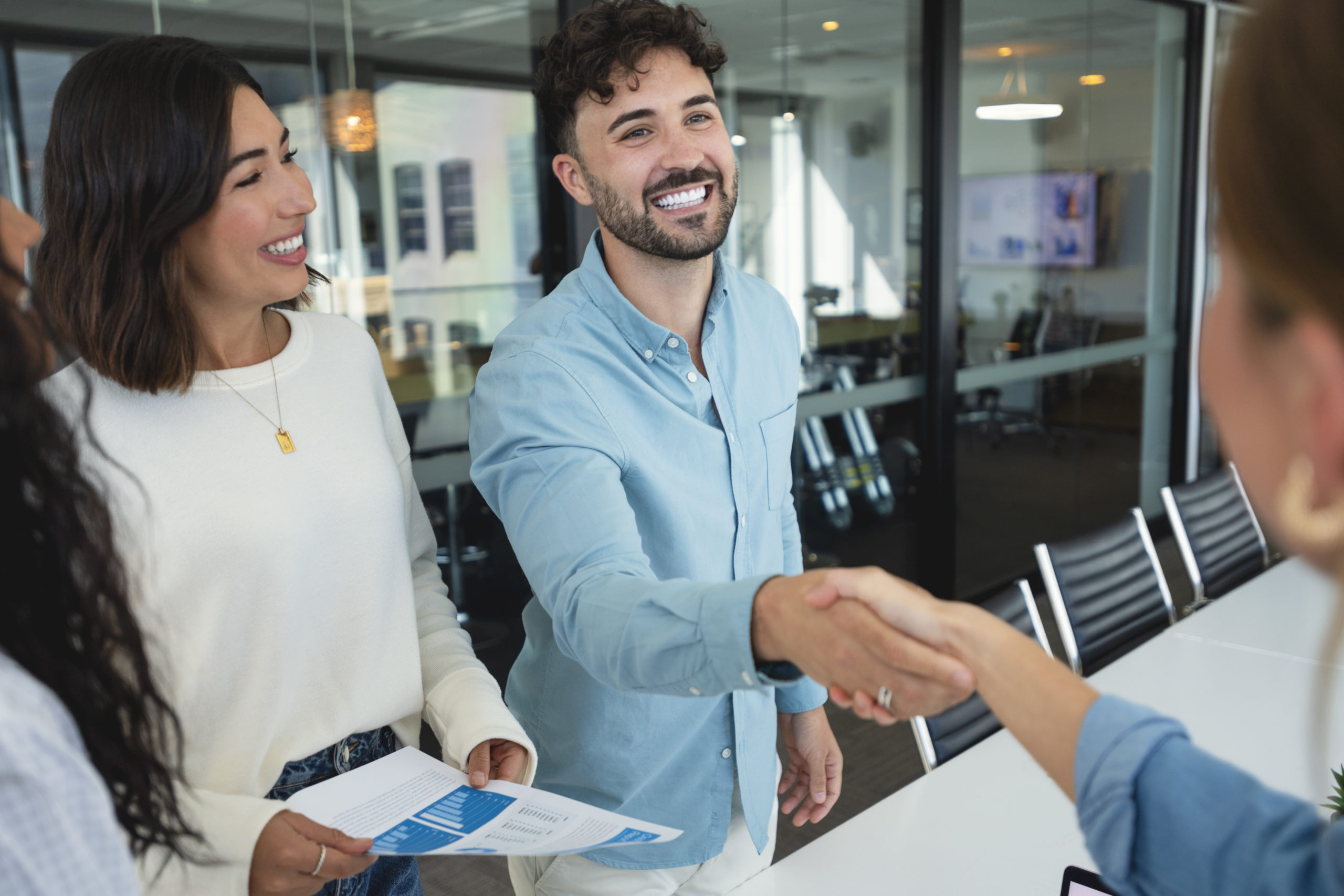 Group of business people greeting each other shaking hands in an office. There is a young man and a young woman. Everyone is smiling and happy