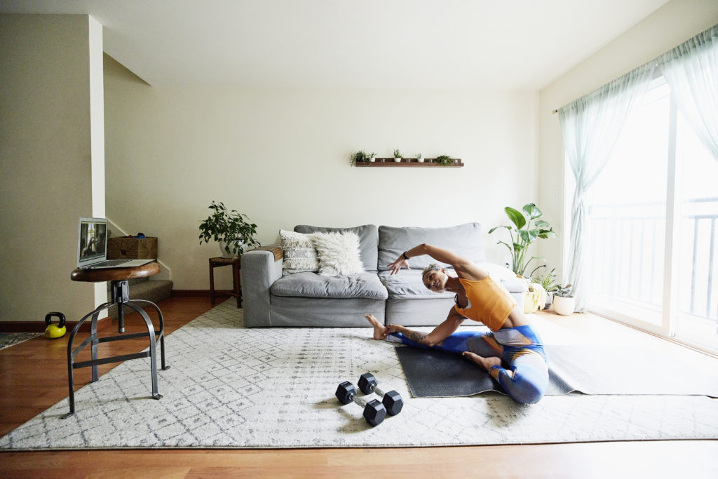 Fitness instructor stretching while leading virtual fitness class from living room