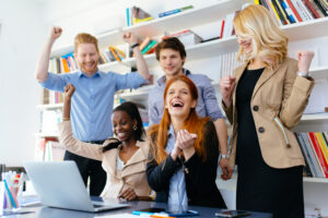 A group of employees crowded around a lap top celebrating a big win, thanks to outsourced HR 