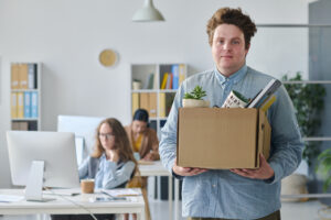 White man with ginger hair leaving his office with a box of his belongings having been fired from his position at an SME business that outsourced it's HR