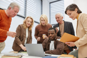 People gathered around a computer in an office of an SME business discussing whether to outsource HR