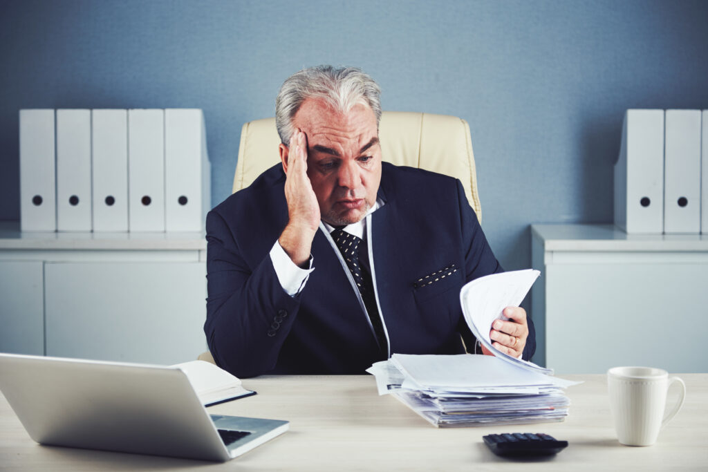 Middle aged business owner with his head in his hand, worried about the expenses on his desk and grappling with the top misconceptions about HR