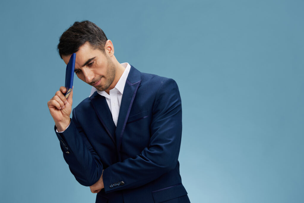 A business owner tapping his head with his phone, trying to think of where to start having seen the signs that he needs to outsource his company's HR